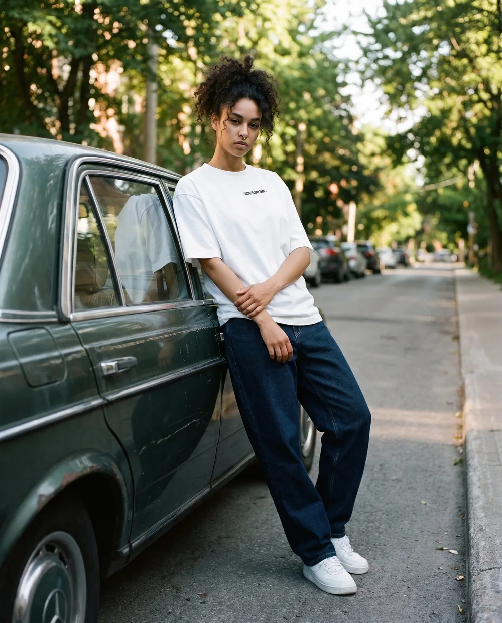 Leaning on an old green sedan on a tree-lined street