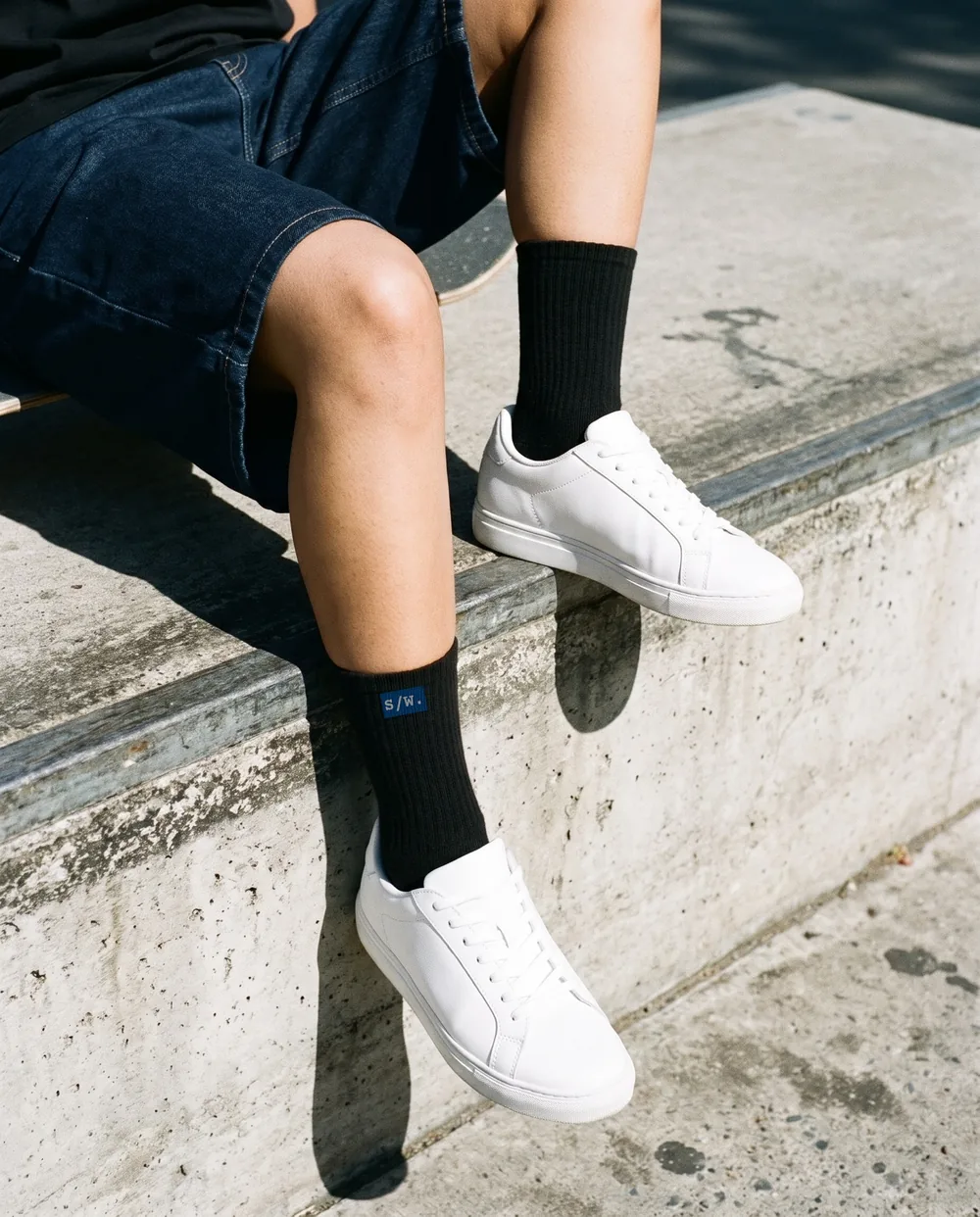 Black crew socks and white sneakers on a concrete ledge
