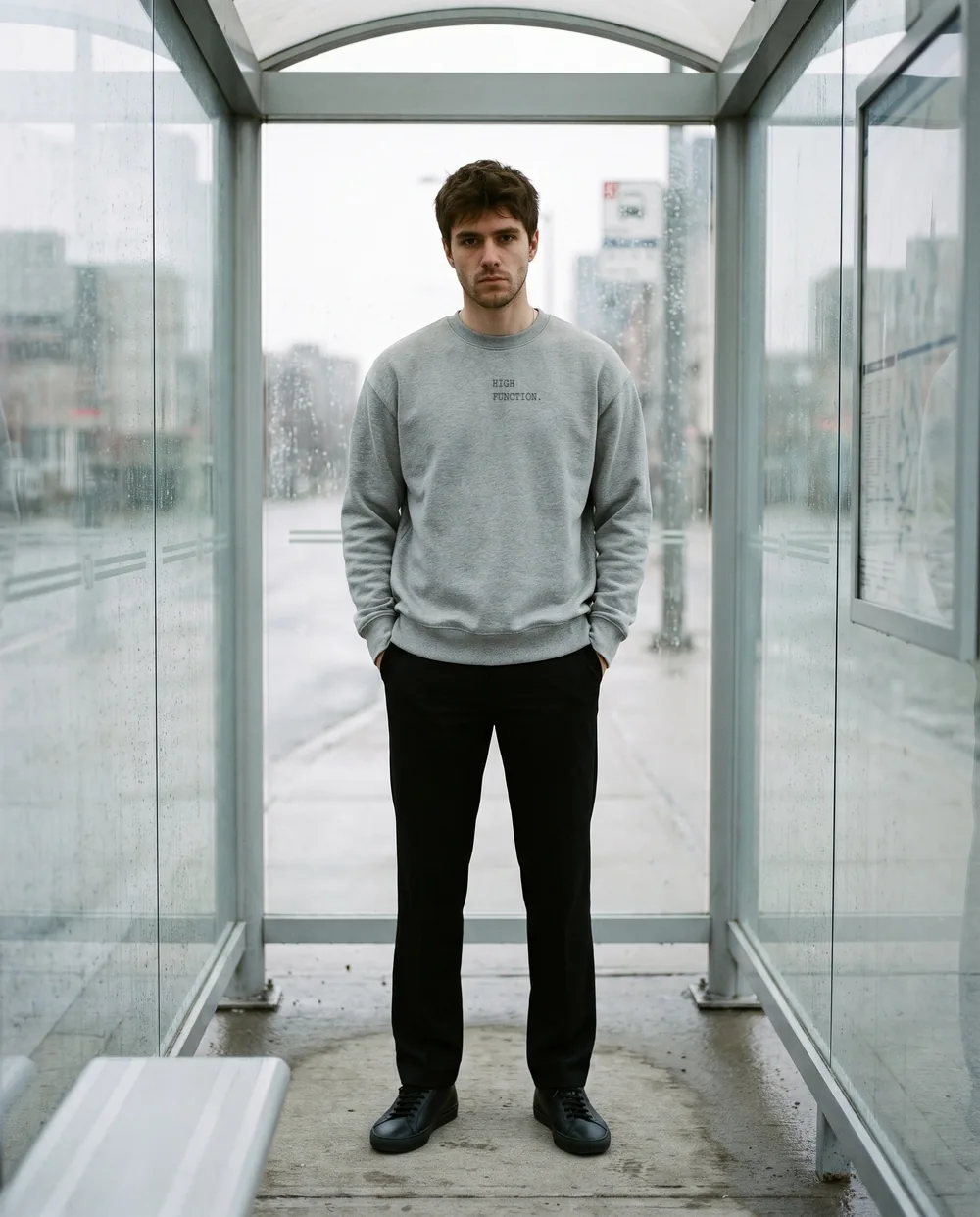 Waiting in a glass bus shelter in a grey crewneck